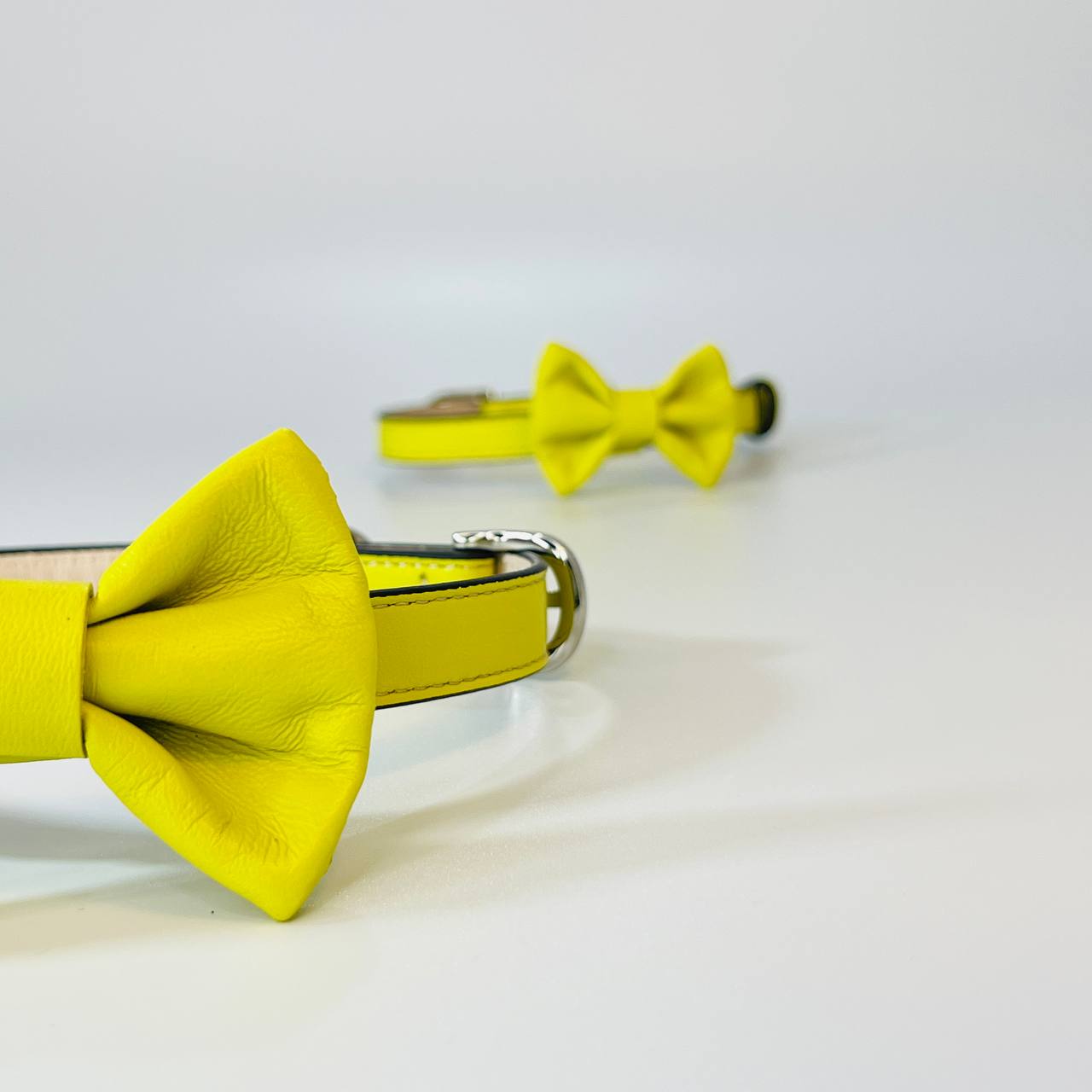 Yellow leather dog collar with bow designs on a light gray background
