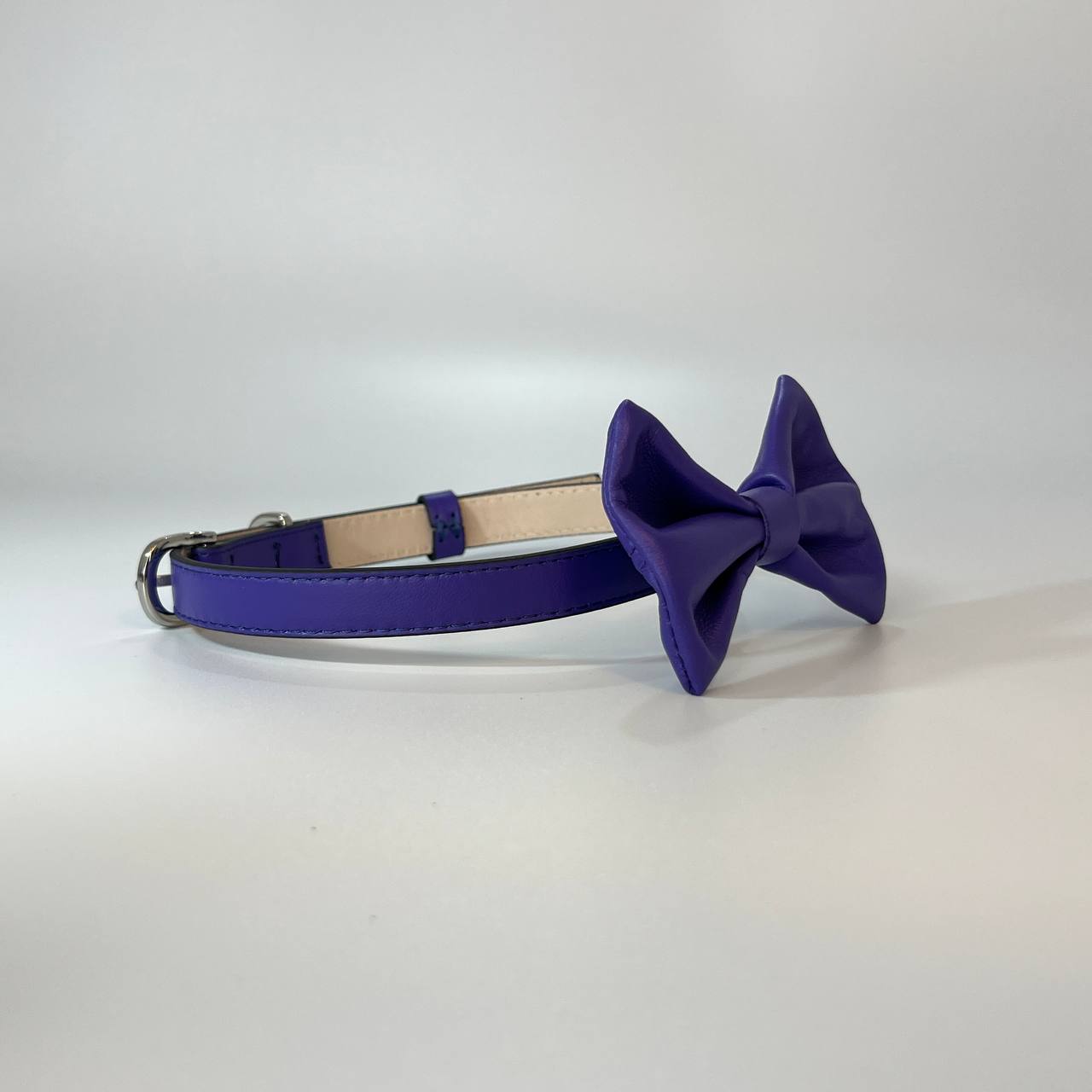 Purple dog collar with a matching bow on a light gray background